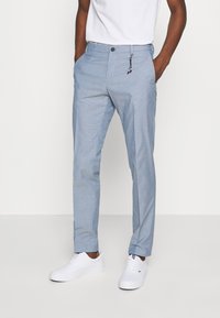 Pantalon à motifs bleu clair avec une coupe ajustée, doté d'une fermeture à bouton et zip, ainsi que de poches. Assorti à des baskets blanches.