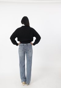 Maglione corto nero a maglia con texture a costine, abbinato a jeans dritti a vita alta blu chiaro e scarpe con tacco beige.
