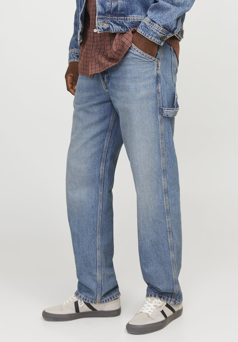 Jean en denim bleu clair avec une coupe droite, doté de poches latérales, d'une coupe décontractée et d'une texture légèrement délavée. Porté avec des baskets grises.