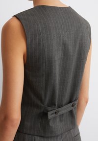 Sleek vest in dark gray fabric with narrow vertical stripes. Features a high neckline, sleeveless design, and a double-button back detail.