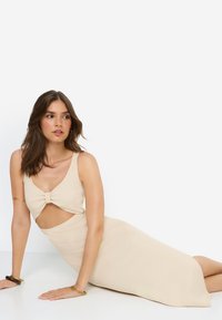 Μπεζ φόρεμα με λεπτομέρεια κοψίματος και φιόγκo στο στήθος, κατασκευασμένο από ριμπ ύφασμα. Διαθέτει φαρδιές τιράντες και εφαρμοστή σιλουέτα.