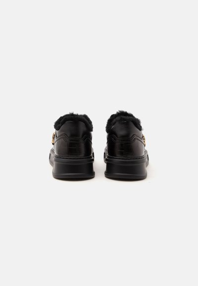 Paire de mocassins en cuir noir avec doublure en fourrure et boucle dorée, présentés de dos sur fond blanc uni.