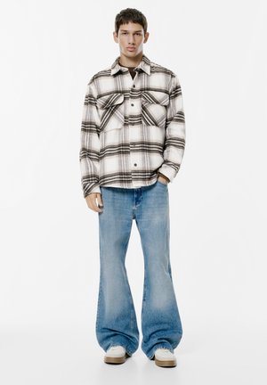 Giacca di flanella a quadri bianca e nera con due tasche sul petto, abbinata a jeans a gamba larga azzurri e sneaker bianche.