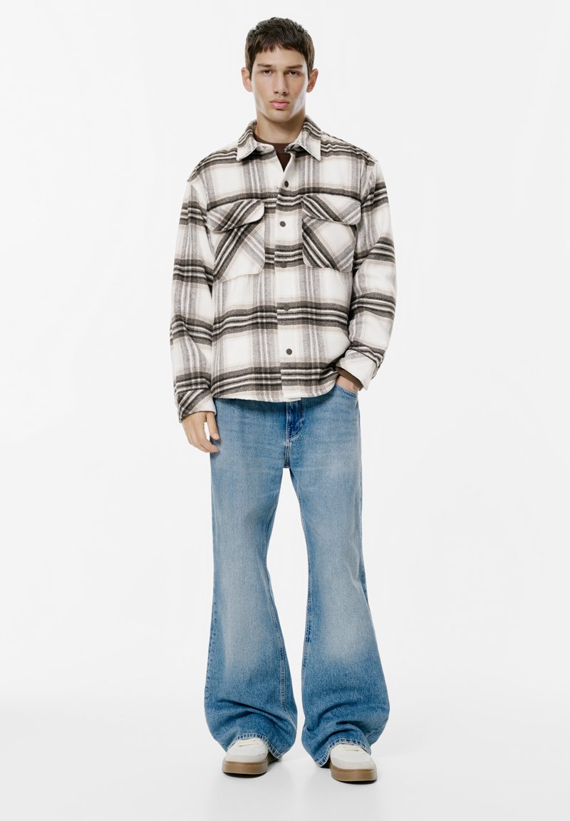 Giacca di flanella a quadri bianca e nera con due tasche sul petto, abbinata a jeans a gamba larga azzurri e sneaker bianche.