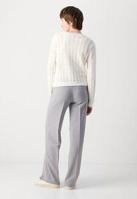 Gehäkelter weißer Pullover mit strukturiertem Muster und gewellten Saum, kombiniert mit grauen, maßgeschneiderten Hosen. Weicher Stoff, lange Ärmel und lockere Passform.