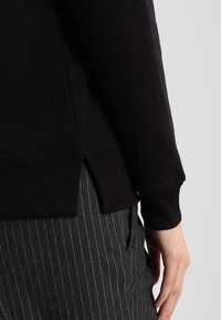 Felpa nera con polsini a coste, dotata di una fessura laterale all'orlo. Texture morbida con una vestibilità comoda, abbinata a pantaloni a righe.