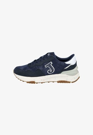 Zapatilla deportiva azul marino con parte superior de ante y tejido, acento blanco en el talón, suela de goma y media suela texturizada con manchas coloridas.