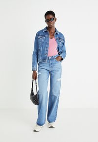 Jachetă din denim, albastră deschisă, cu buzunare tip patch și guler contrastant; cămașă roz cu decolteu în V; blugi largi, albastru deschis, cu detalii uzate; geantă neagră.