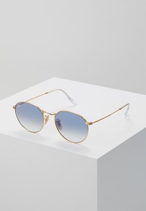 Occhiali da sole in metallo dorato con lenti rotonde a gradiente blu, aste sottili e terminali trasparenti. Design minimalista con un dettaglio di branding discreto.
