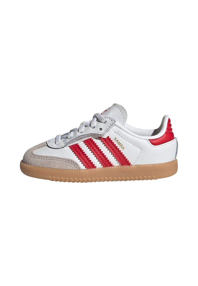 White leather sneakers with red accents, three red stripes, and tan rubber outsole. Features a suede toe cap and gray laces.