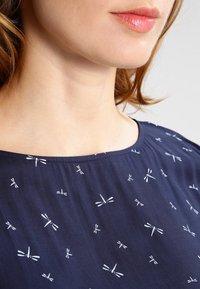 Námořnická blůza s bílým vzorem vážek, kulatým výstřihem, měkkou tkaninou a nařasením na ramenech.