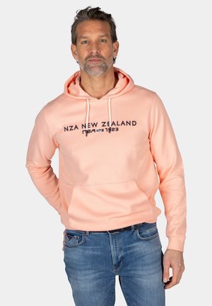 Lichtroze hoodie met een voorvak, voorzien van een donkerblauwe logo-tekst. Het materiaal lijkt zacht en heeft een lichte textuur.