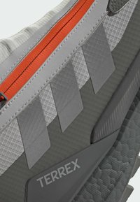 Gray hiking shoe featuring a textured finish, orange zipper, layered gray accents, and prominent TERREX branding. Durable materials used.