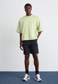 T-shirt oversize vert clair, shorts cargo noirs avec poches, et baskets blanches. Tissu texturé et coupe décontractée. Tenue décontractée.