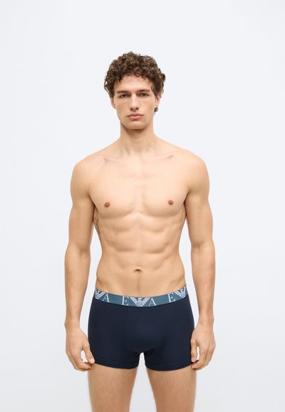 Bokserice tamnoplave boje od mekanog tkanja, s kontrastnim elastičnim pojasom s logotipom, uskog kroja i glatke teksture.