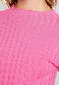 Primo piano di una persona che indossa un maglione a coste rosa con scollatura grezza, mostrando la parte superiore della schiena e del collo.