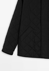 Gequilte zwarte jas met een soepele textuur, voorzien van diagonale stiksels, een zijzak en een ritssluiting aan de onderkant van de mouw.