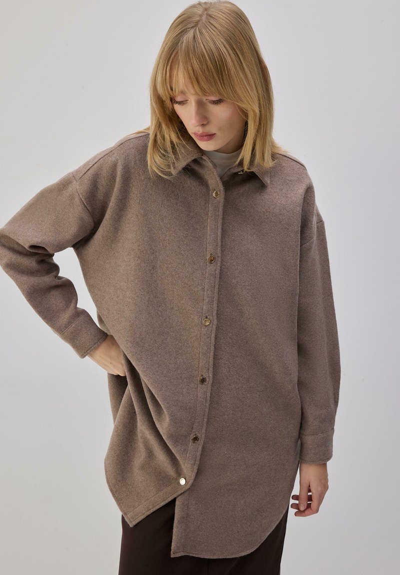 Pruun villane särk, millel on nööpidega eesmine osa, klassikaline krae, liialdatud suurus ja kõveralt lõigatud serv. Silmapaistev sile tekstuur ja õrn läige.