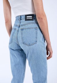 Ljusblå denimjeans med hög midja, raka ben och synlig sömnad. Har två bakfickor och en svart etikett med "DRDENIM".