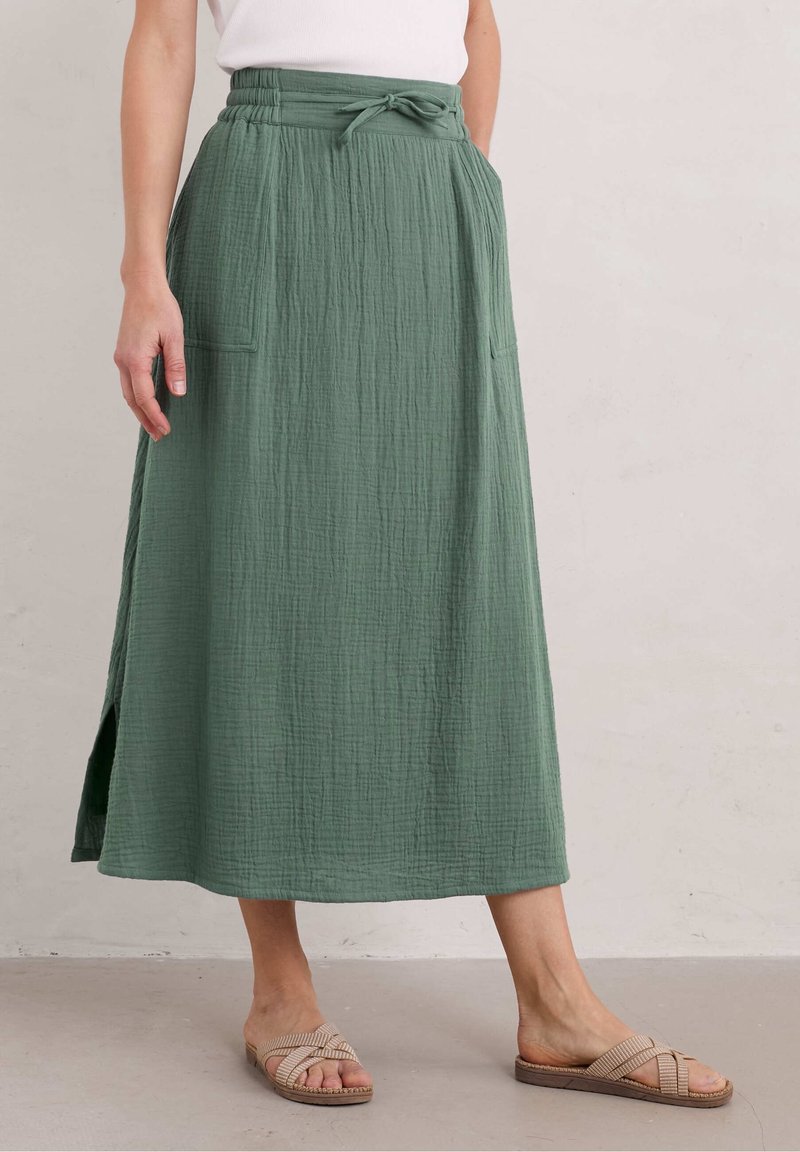 Gonna maxi verde in tessuto stropicciato con vita regolabile, due tasche laterali e uno spacco laterale, abbinata a sandali piatti marrone chiaro.