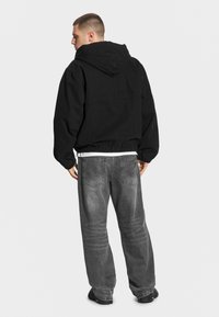 Czarna kurtka z kapturem z elastycznym dołem, noszona na białej koszuli, zestawiona z luźnymi szarymi dżinsami. Gładki materiał i minimalistyczny design.