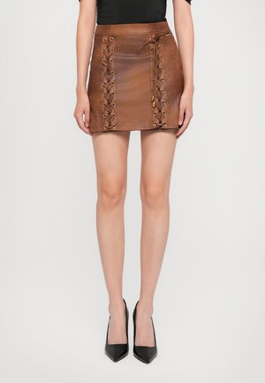 Mini-jupe en cuir marron avec laçage sur les côtés et œillets dorés ; texture lisse avec un léger éclat ; accompagnée de chaussures à talons hauts noires.