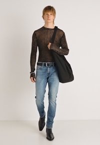 Top castanho texturizado de manga comprida com design ajustado, combinado com jeans azuis claros e botins pretos, a carregar uma bolsa preta.