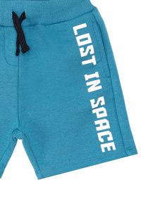 Pantalones cortos de algodón azules con una cinturilla acanalada, con un cordón negro y texto impreso en blanco "PERDIDO EN EL ESPACIO" en el lado.