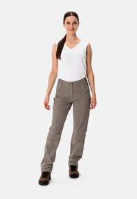 Pantaloni da trekking leggeri, beige, con cintura elasticizzata, tasche laterali e vestibilità affusolata, indossati con un top bianco senza maniche e scarpe marroni.