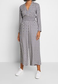 Mono con estampado navy de manga larga, escote en V, cintura fruncida y silueta de pierna ancha, combinado con zapatillas blancas.
