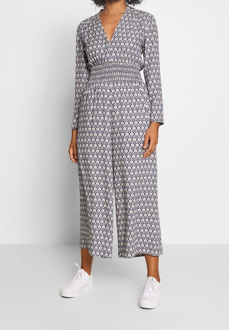 Mono con estampado navy de manga larga, escote en V, cintura fruncida y silueta de pierna ancha, combinado con zapatillas blancas.
