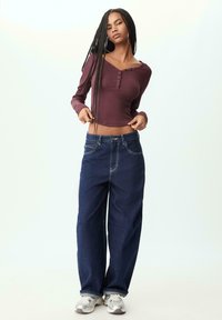 Maroon long-sleeve top with a button detail paired with high-waisted wide-leg blue jeans and silver athletic shoes. Smooth fabric textures.