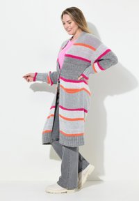 Cardigan grigio a maglia con audaci strisce rosa, arancioni e bianche. Presenta maniche lunghe, un orlo a coste e tasche frontali. Indossato sopra una maglietta rosa.