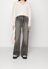 Suéter de color rosa claro, de gran tamaño y con escote en "v" hecho de una tela suave, combinado con unos jeans de tiro alto, de pierna ancha y en negro desgastado, junto a un pequeño bolso beige texturizado.