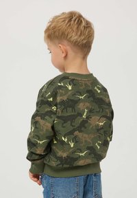 Zielona bluza w kamuflażu z sylwetkami dinozaurów w kolorze czarnym i żółtym. Żebrowany okrągły dekolt i mankiety; miękka tkanina, swobodny krój.