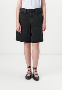 Black denim shorts with a loose fit, featuring a button closure and five pockets. Worn with a light blue striped shirt and black lace-up flats.