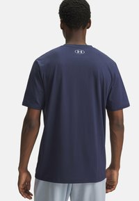 Granatowa koszulka z krótkim rękawem uszyta z miękkiego materiału, z okrągłym dekoltem i logo Under Armour z tyłu. Projekt jest prosty i minimalistyczny.