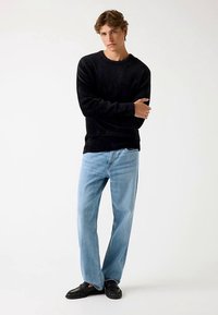 Pulover negru texturat, blugi largi bleu deschis și mocasini negri. Modelul pozează cu brațele încrucișate, prezentând o ținută casual.