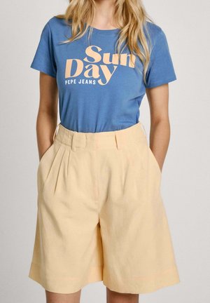 Kobieta nosząca niebieską koszulkę z tekstem "Sun Day Pepe Jeans" oraz beżowe, szerokie szorty z wysokim stanem i kieszeniami.