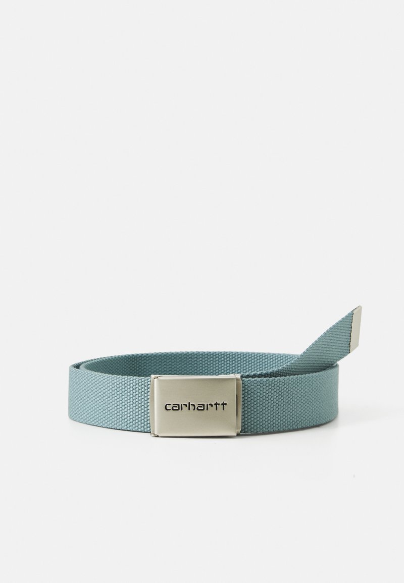 Curea din țesătură albastră cu o suprafață texturată, având o cataramă metalică argintie gravată cu numele brandului "Carhartt."