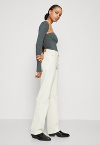 Top gris de manga larga ajustado combinado con jeans blancos de pierna ancha y botines negros, resaltando un ajuste entallado y texturas suaves.
