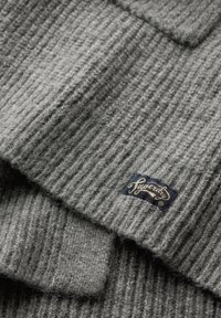Gray knitted sweater with textured ribbing, featuring a folded collar and a fabric label in blue and gold at the bottom right corner.