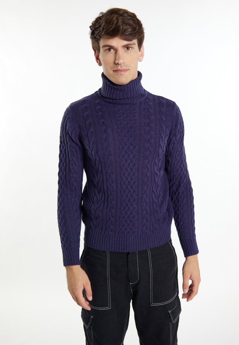 Maglione a collo alto color navy con motivo a trecce, polsini e orlo a costine. Indossato con pantaloni cargo neri. Texture liscia, design aderente.