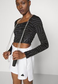 Svart langermet crop topp med zebra mønster, sammen med en hvit plisserte skorts med Adidas-logo. Hoppetau i hendene.