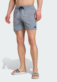 Prúžkované modré plavky s elastickým pásom a námorníckou šnúrkou; obsahujú malé logo na dolnej ľavej nohe. Nosí sa s šľapkami.