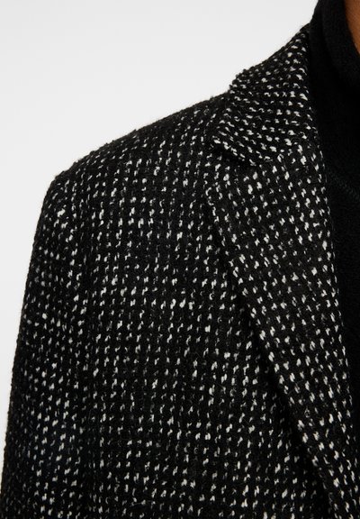Zwart-witte houndstooth blazer met een gestructureerde stof, voorzien van een notch-kraag en gestructureerde schouders, die een klassiek patroon toont.