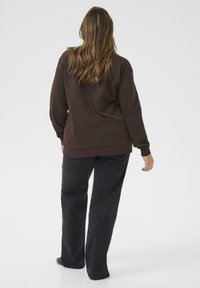 Felpa marrone con scollatura tonda e spalle drop, abbinata a pantaloni neri a gamba dritta. Tessuto morbido con dettagli di design minimi.