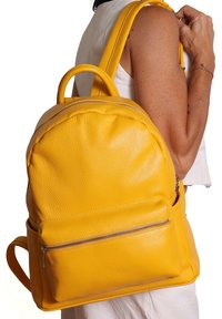 Vista spalla di una persona che porta uno zaino in pelle gialla brillante con una tasca frontale con zip e manico superiore.