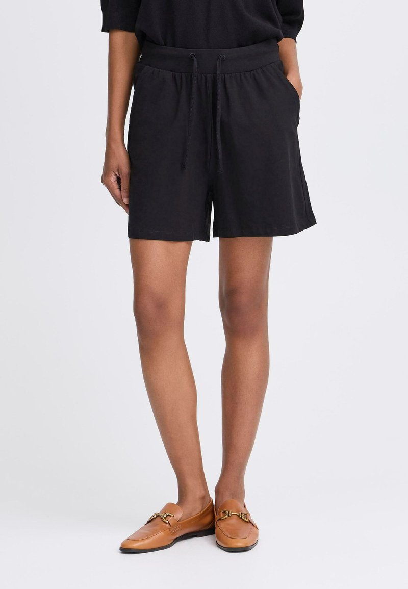 Shorts noirs à cordon de serrage avec une taille élastique, dotés de poches latérales et d'une coupe décontractée. Associés à des mocassins bruns.