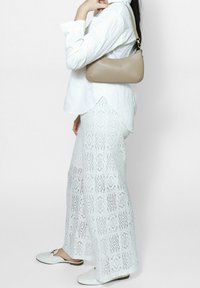 Witte kanten maxi rok met geometrische patronen, gecombineerd met een losse witte button-up blouse en een beige leren handtas. Witte instappers.
